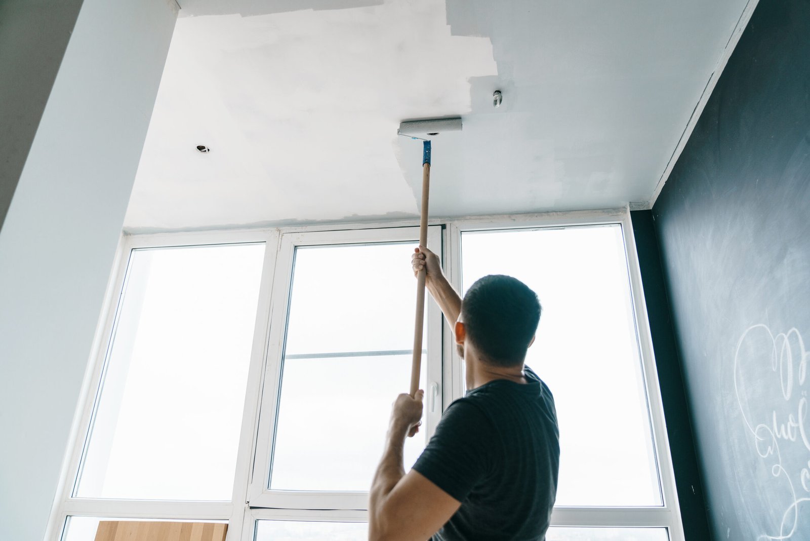 the man paints the walls and the ceiling in gray color, standing with his back to the camera. Focus on the roller. Painting and repair of the room.
