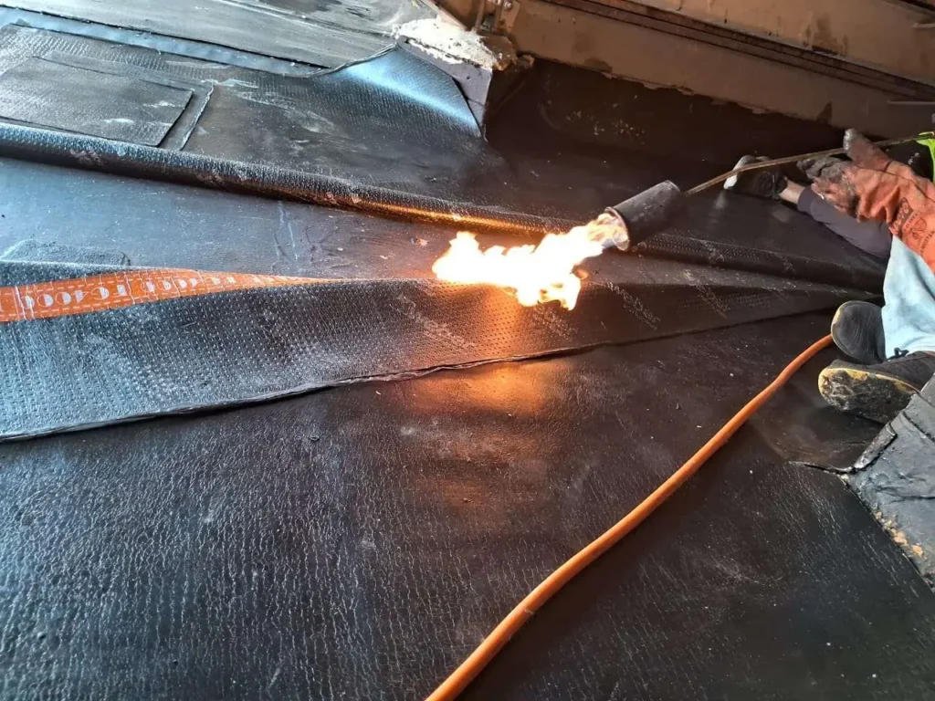 Technician heat-welding a torch-on bitumen membrane on a Dubai villa roof