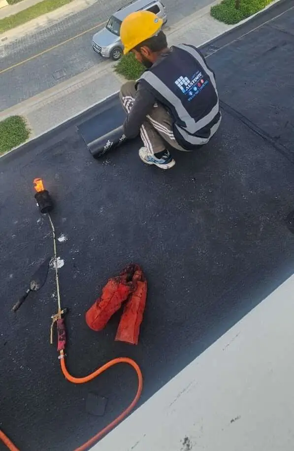 Technician laying bitumen membrane on a primed roof • #1 Waterproofing Company in Dubai & UAE • #1 Waterproofing Company in Dubai & UAE Technician laying bitumen membrane on a primed roof